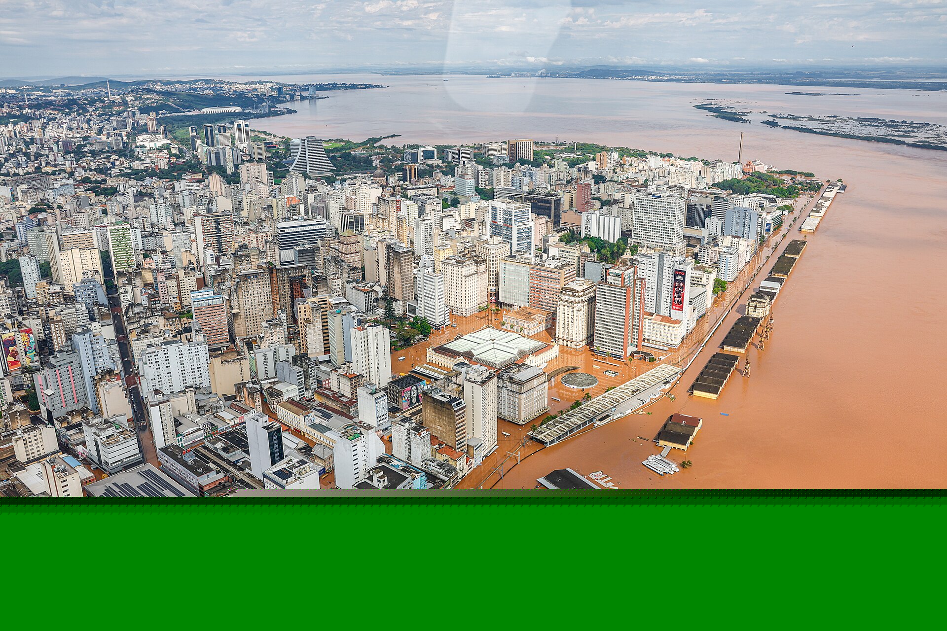 An aerial image of flooding in Canaos, Rio Grande do Sul. Light brown water overflows from a river delta into a city, flooding roads and surrounding buildings.